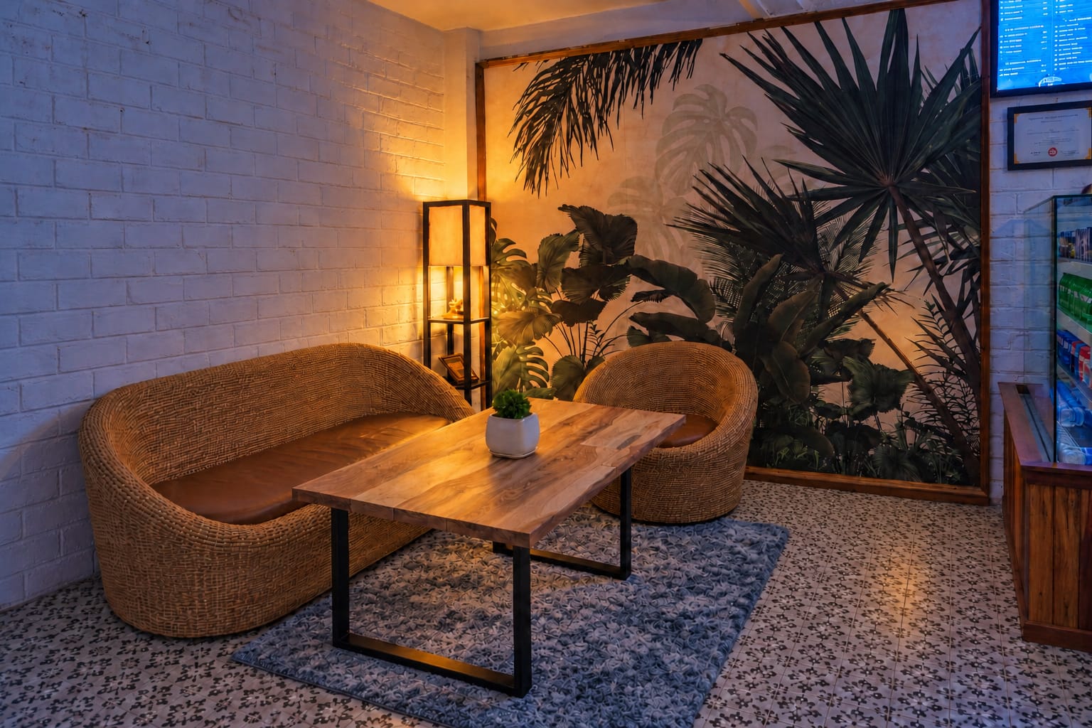 Two woven wicker seats and a wooden table on a blue-grey rug, beside a palm mural and a floor lamp